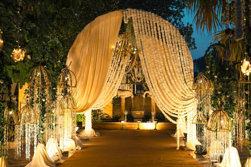Floral garland arch entrance with gold birdcage lanterns at Bali Pool Side, Mallu Farms Chattarpur